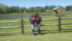 Enjoying a sunny day outdoors at a farm with a wooden fence and lush green fields.