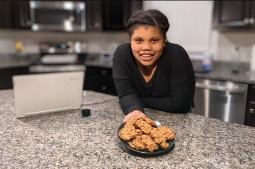 A girl smiling at a plate of fried chicken on a kitchen countertop.