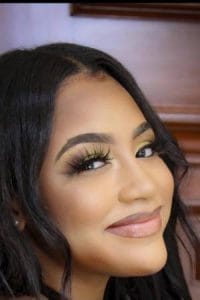 Portrait of Kyra Pierce with long dark hair and thick eyelashes smiling sideways