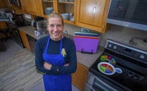 Healthy woman smiling in kitchen wearing blue apron, preparing food or cooking.