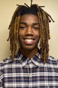 Bright young man with dreadlocks smiling, wearing a checkered shirt, representing diversity and yout.