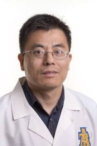 A doctor in a white lab coat with a hospital logo, looking confidently at the camera.