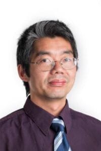 A person wearing glasses and a dark purple shirt with a striped tie, professional portrait.