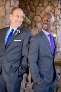 A smiling couple in formal suits at a wedding celebration.