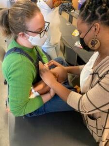 Administering a vaccination to a young girl in a healthcare setting, with medical staff and equipmen.