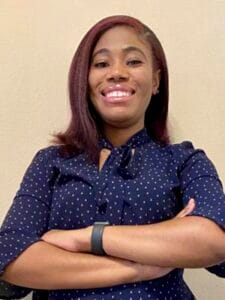 A woman smiling confidently with crossed arms, wearing a navy blue polka dot blouse.
