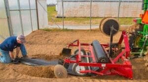 Man bending down behind a tractor laying down plastic for plants.