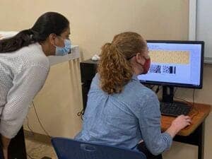 A woman and a girl working together on a computer in an office setting, both wearing masks.
