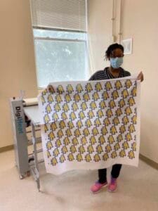 Person wearing a face mask holding a large printed fabric with yellow and black patterns.