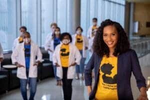 A woman leading a diverse group of healthcare professionals in a modern hospital corridor.