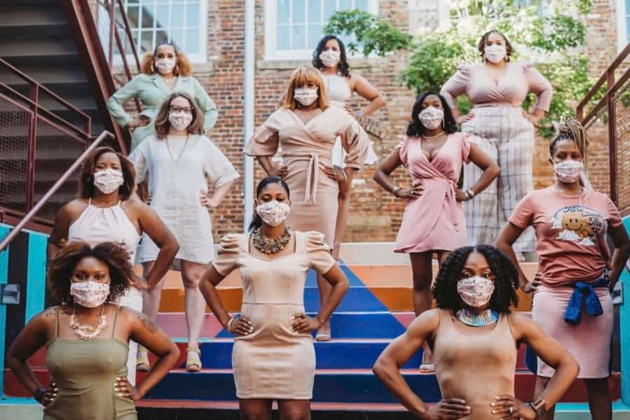 A woman-led diverse group of women wearing face masks standing confidently on outdoor stairs.