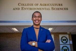 A young man in a blue blazer smiling outside the College of Agriculture and Environmental Sciences.