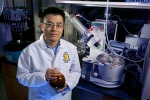 A scientist in a laboratory holding a flask with a dark liquid, surrounded by scientific equipment.