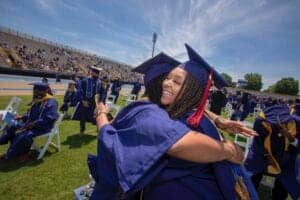 Graduates celebrating at a graduation ceremony on a sports field, wearing caps and gowns, with a joy.