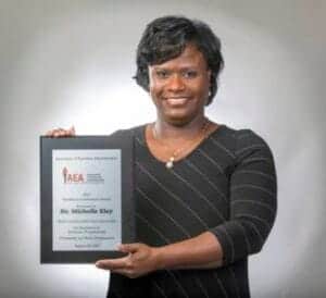 A woman holding a framed certificate, smiling confidently.