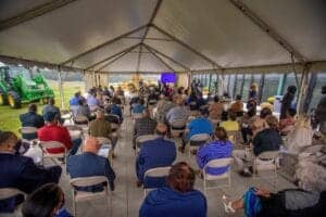 Outdoor conference under a large tent with attendees watching a presentation on a big screen.
