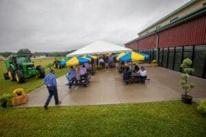 Outdoor event with people gathering under yellow and blue umbrellas at a farm or agricultural venue.