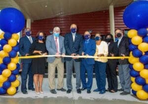 Brightly dressed officials at ribbon-cutting ceremony with blue and yellow balloon decorations.