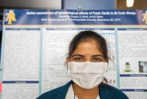 A woman wearing a face mask standing in front of a scientific research poster.