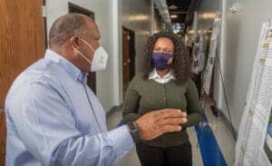 COVID-19 safety measures discussion between two professionals in an office hallway.