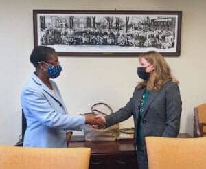 Two women wearing masks shaking hands in an office setting.