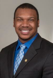 A smiling man in a business suit with a blue shirt and patterned tie, professional portrait.