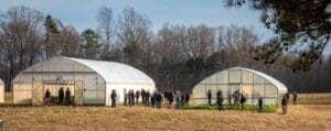 Greenhouse structures with people gathering outdoors in a rural setting.