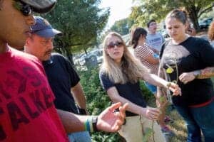 A woman explaining plant care to a group outdoors during a community event.