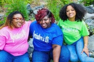 Empowered women smiling outdoors in colorful t-shirts, promoting confidence and community.