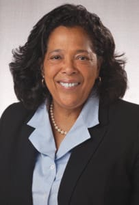 A woman in professional attire smiling, wearing a black blazer and pearl necklace.