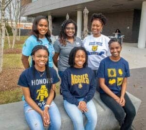 Empowered women students wearing Aggies and college pride apparel outdoors at campus.