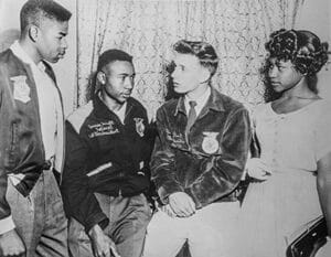 A woman in a police uniform talking to three young people in a room with patterned curtains.