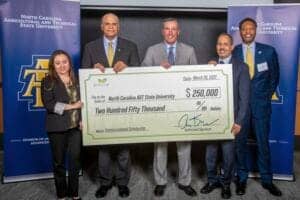 Empowered individuals holding a large scholarship check at North Carolina A&T State University event.