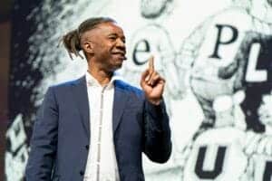 Confident male speaker presenting at CAES News event with a background of abstract graphics.