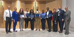 Empowered diverse professionals at CAES News conference holding certificates for recognition.