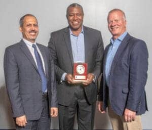 A man receiving an award from two colleagues at a professional event.