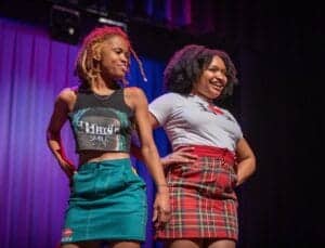 Brightly dressed women smiling on stage during a live event at CAES News.