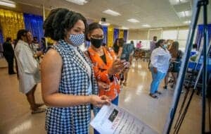 Women at a conference viewing a smartphone and event information display.