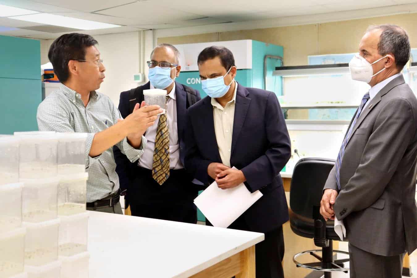 Business professionals in a laboratory discussing scientific research, wearing masks for safety.