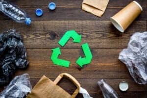 Recycling symbol on wooden surface with trash and bottles, environmental awareness concept.