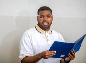 A person reading a blue book, wearing glasses and a white polo shirt with beige collar.