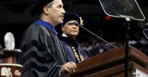 Graduation ceremony with academic regalia and speakers at the podium.