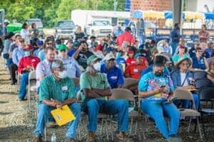 Voters attending outdoor community event wearing masks and seated in rows.