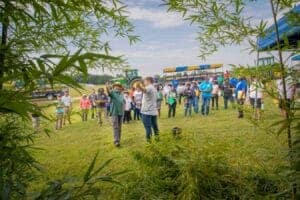 Plantation event with people gathering outdoors on a sunny day, trees and greenery in the foreground.