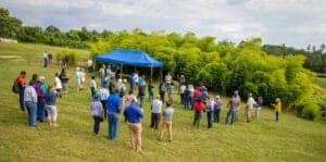 Accessible outdoor community gathering with people standing on grass near a blue tent and lush green.