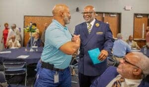 Two men shaking hands at a professional event in a conference room.