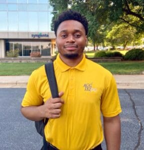 Innovative young man in yellow polo shirt with "AGG" logo outside corporate building.