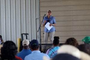 Woman speaking at outdoor event with microphone and audience in attendance.