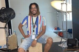 A man with dreadlocks and glasses smiling in a photography studio with professional lighting equipme.
