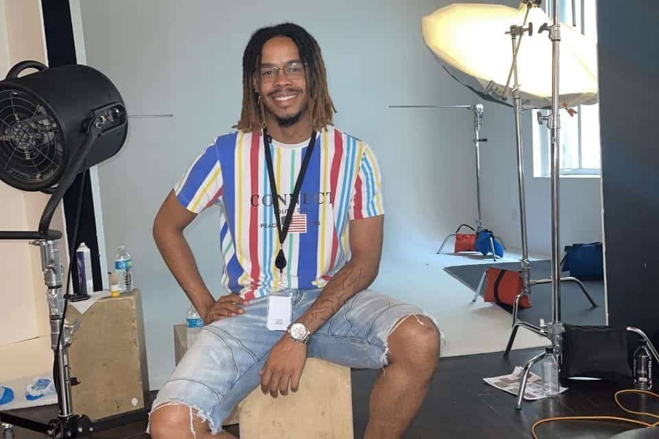 A man with dreadlocks and glasses smiling in a photography studio with professional lighting equipme.